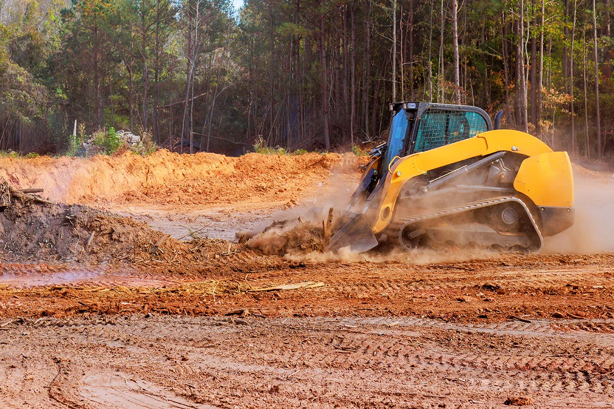Compact track loader clearing brush and grading soil on a job site